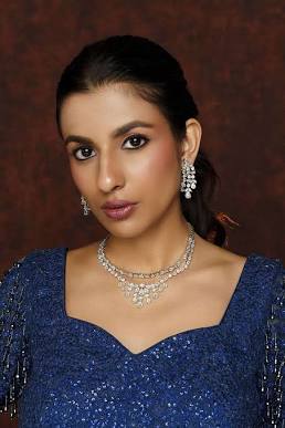 Portrait of a woman wearing a blue sequined gown, a diamond jewelry necklace and earrings, looking at the camera.