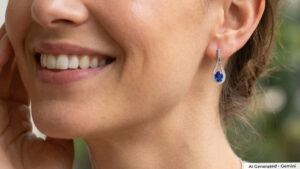Close-up of a woman's smiling face, showing a blue teardrop gemstone earring in her ear.