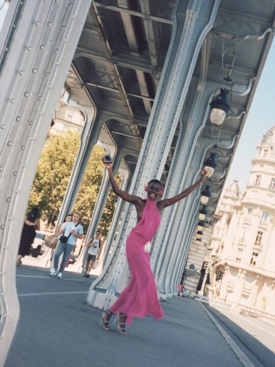 Nué Studio’s Fall/Winter 2025 collection introduced the “Daphne” dress in vivid fuchsia pink, a backless, semi-sheer chiffon creation made from silk crepe georgette and detailed with a halter neckline, draped bodice, carré open back, crystal hip brooch, and dramatic side slit