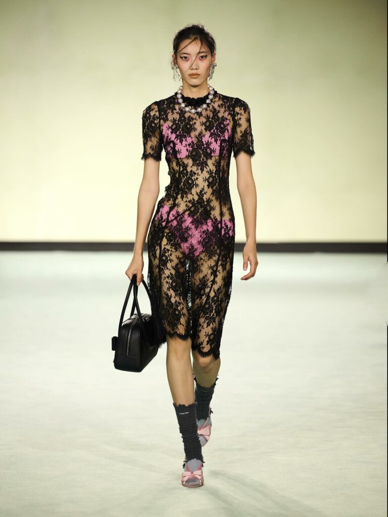 Shushu/Tong’s Spring/Summer 2026 collection featured a sheer black, short-sleeved gossamer dress embellished with floral lace, worn over a bubblegum-pink two-piece set consisting of a balconette bra top and high-waisted briefs