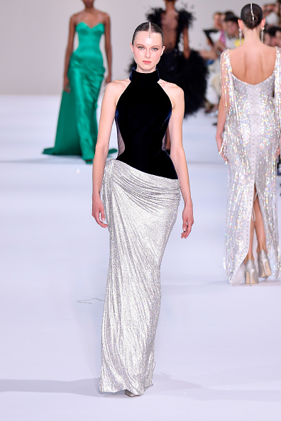 Tamara Ralph’s Haute Couture Fall/Winter 2026–2027 collection featured a black velvet halter top detailed with sheer mesh side and back panels, paired with an asymmetrically draped skirt made of silver crystal mesh—a look singer Taylor Swift chose for her appearance at the 2026 MTV Video Music Awards.