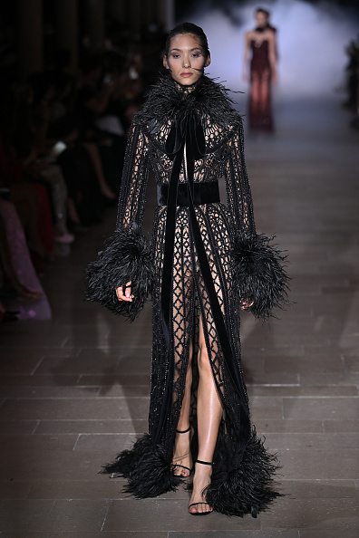 Zuhair Murad’s “Love and Dominion” Haute Couture Fall/Winter 2026/2027 collection featured a black mesh coat-gown cinched with a belt and adorned with feather plumes at the high collar, cuffs, and hem