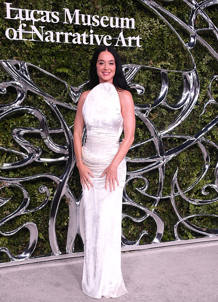Katy Perry stepped out for the opening night of the Lucas Museum of Narrative Art in a Christian Siriano white crushed-velvet column gown featuring an asymmetric sculpted neckline and back slit, styled with René Caovilla “Ellabrita” silver sandals.