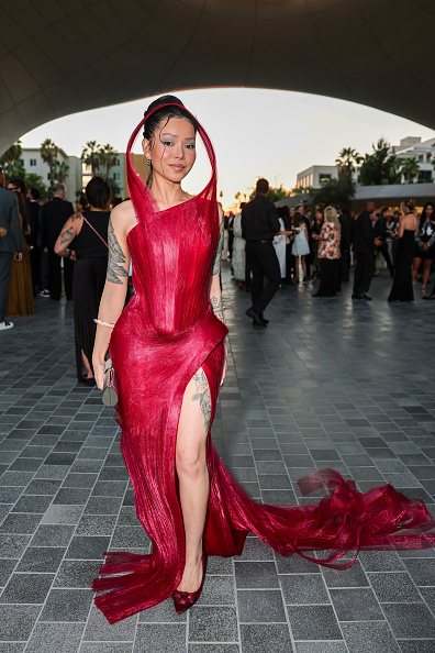 Bella Poarch wore matching deep-crimson, pointed-toe satin pumps adorned with ribbon bows, a metallic silver cylindrical evening bag, gold cuff bracelets