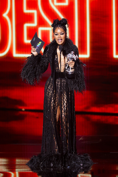 Teyana Taylor captivated onlookers in a sophisticated, fashion-forward black mesh coat gown embellished with feather plumes along the collar, cuffs, and sweeping floor-length hem.