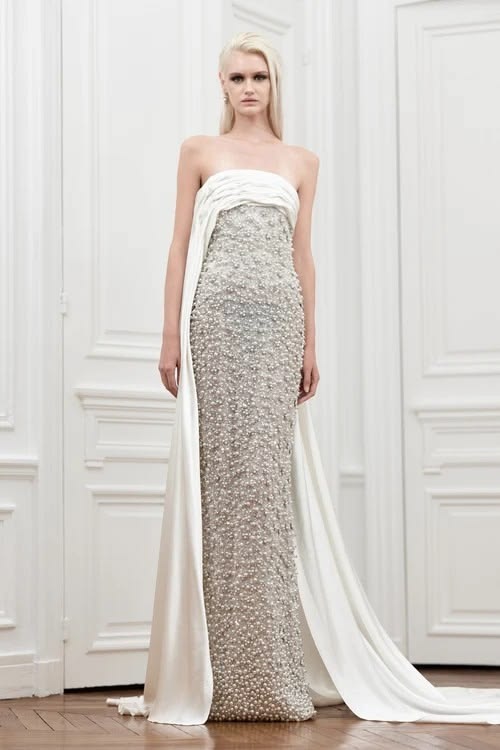 Yara Shoemaker’s “Precious” Fall/Winter 2026/27 collection presented a strapless gown embellished with pearls and crystals, paired with a floor-length tulle sash and later reimagined for Leonie Hanne’s appearance at the 2026 Venice International Film Festival.