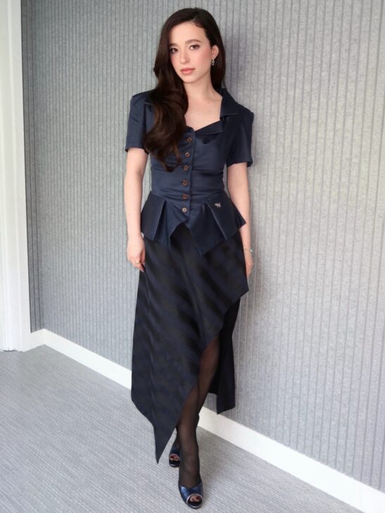 Mikey Madison was photographed in London during the press tour for “The Social Reckoning,” dressed in a Vivienne Westwood “Monday” cotton top and a striped “Cassandre” midi skirt crafted from virgin wool, complemented by Tiffany & Co. jewelry.