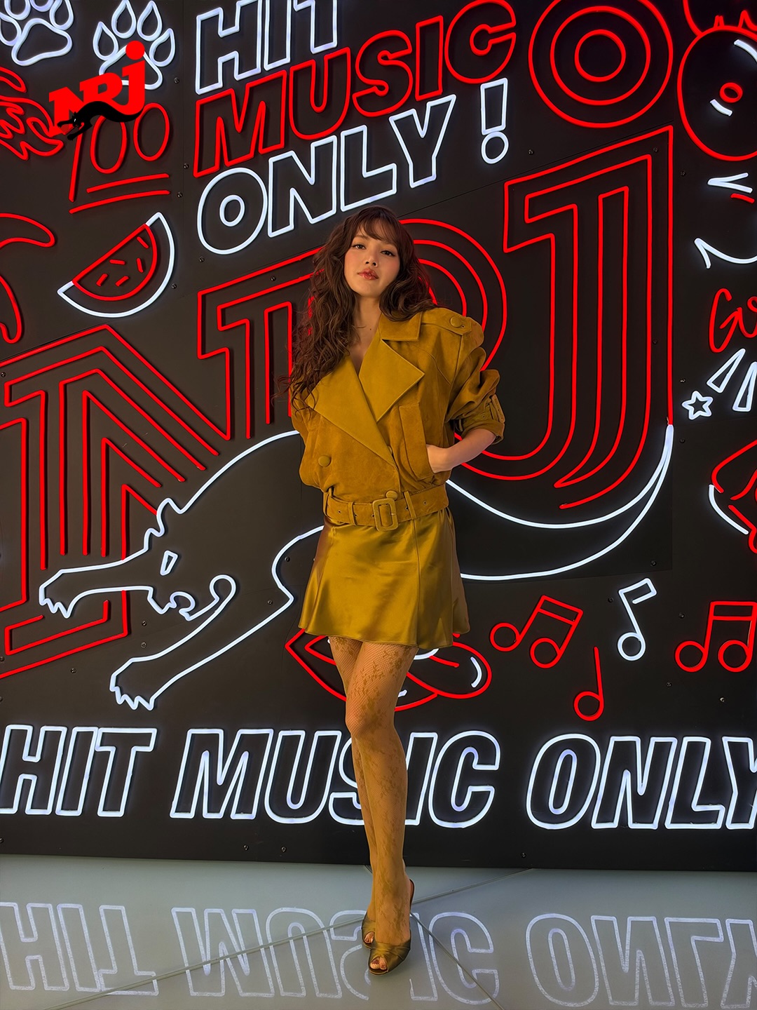 Her jacket was styled with a matching “Bonny” ochre sleeveless A-line satin slip dress, distinguished by a deep V-neckline edged in sheer Chantilly lace along the straps and center bodice, drawing inspiration from Retrofête’s Fall/Winter 2026 “La Société d’Opulence” collection.