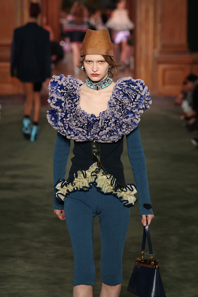 Louis Vuitton’s Cruise 2027 collection presented a ruffled corset top framed by densely layered, voluminous lilac and purple fabric, evoking clusters of carnation petals around its off-the-shoulder neckline, paired with an asymmetrical pale yellow ruffled piece trimmed in dark edging at the hem