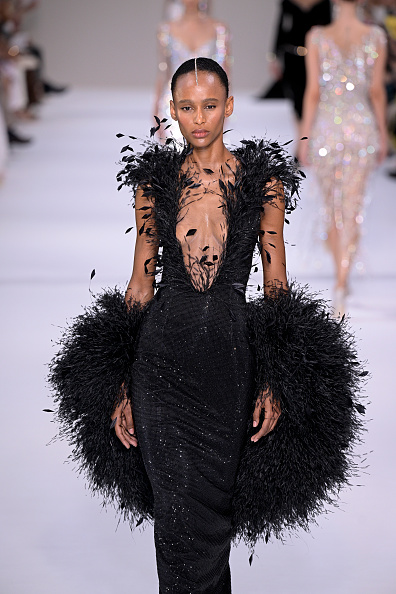 Fashion model Ailiny Marques walked the runway at the Tamara Ralph Haute Couture Fall/Winter 2026/2027 show, presenting a black crystal gown adorned with black dévoré ostrich and diamond coque feathers, styled with a matching black dévoré ostrich feather cape