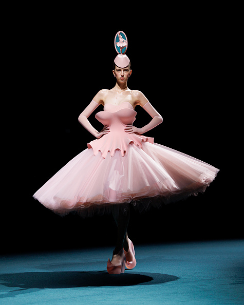 Model Ombeline Suroy walked the runway at Robert Wun’s Haute Couture Fall/Winter 2026/2027 “Childsplay” show in a strapless lace-up gown featuring a double-layer trompe-l’œil bodice, a tiered, ballet-inspired tulle tutu skirt, and a pillbox fascinator topped with a three-dimensional ballerina figurine inside a vertical hoop
