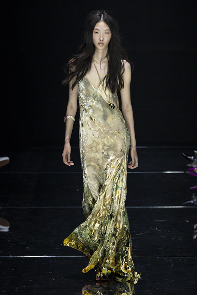 Fausto Puglisi’s Roberto Cavalli Spring/Summer 2027 “House of Prints: The Muses in Los Angeles” ready-to-wear collection featured a backless maxi slip dress with a plunging V-neckline and botanical motif in metallic gold, subdued earthy greens, and rich darker shades, creating a watercolor-like effect along the hem