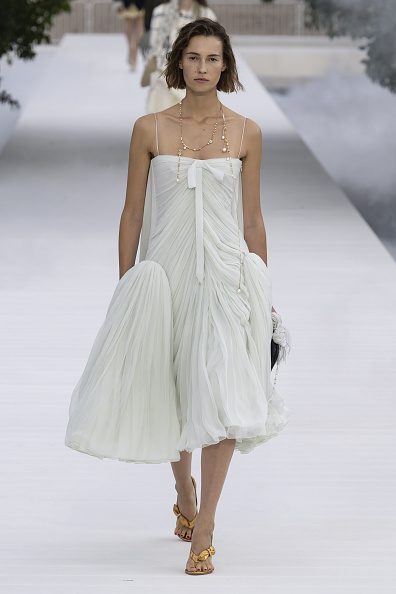 Model Mali Koopman took to the runway for Christian Dior’s Spring/Summer 2027 ready-to-wear show in a sleeveless spaghetti-strap midi dress defined by sculptural side volume, pleated detailing, and a bow tie that cascaded downward