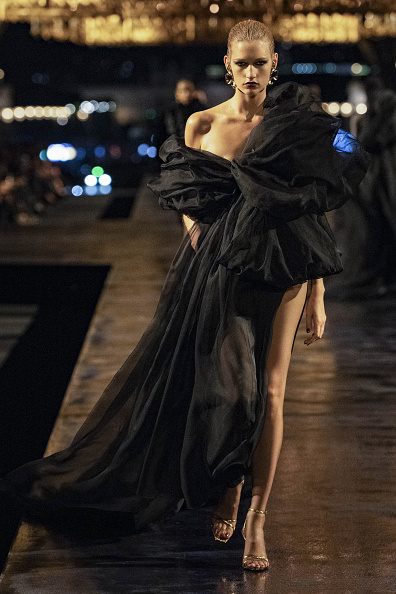 Model Apolline Rocco Fohrer took to the runway at Saint Laurent’s Spring/Summer 2027 ready-to-wear show in a black sheer tulle gown with an off-the-shoulder neckline, an oversized organza bow, and a dramatic slit running from the high waist to the hem