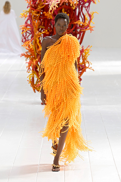 Canadian-South Sudanese model Awar Odhiang walked Balenciaga’s Spring/Summer 2027 Womenswear runway in a tangerine-orange high-low midi dress featuring an asymmetrical one-shoulder silhouette and a dense fringe of tiny bead-like spheres—the same look Tracee Ellis Ross wore to the 2026 Academy Museum Gala.