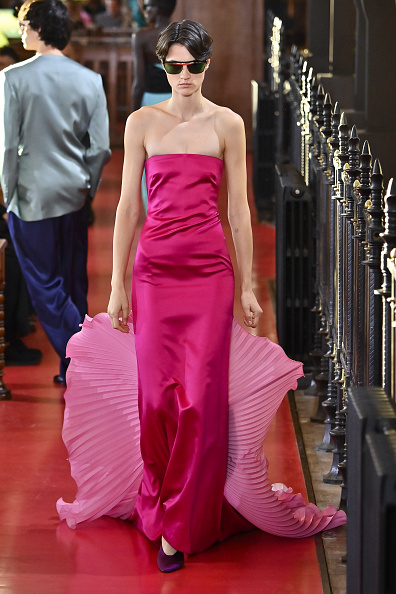 Fashion model Tanya Churbanova walked the runway for Valentino’s Spring/Summer 2027 “Antibiblioteca” (Antilibrary) ready-to-wear show in a strapless fuchsia-pink satin column gown, styled with an oversized panel of pale bubblegum-pink sculptural fabric that trailed from the hem and opened into an exaggerated fan silhouette, accented by pleats and a central black bow motif