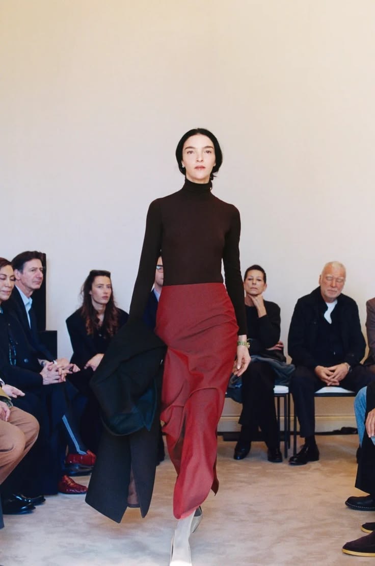Italian model and actress Mariacarla Boscono walked in The Row’s Fall/Winter 2026/2027 ready-to-wear show wearing a deep-plum long-sleeved turtleneck bodysuit styled with a high-waisted ruby-red satin skirt featuring a side slit